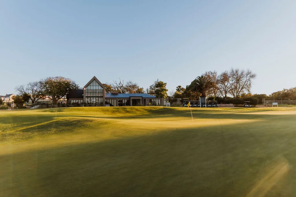 The Malmesbury Golf Club clubhouse beyond a green at sunset